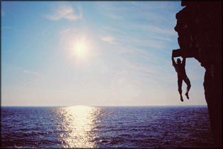 Breaking boundaries: Man hanging from cliff over the sea. Impossible rock climbing.